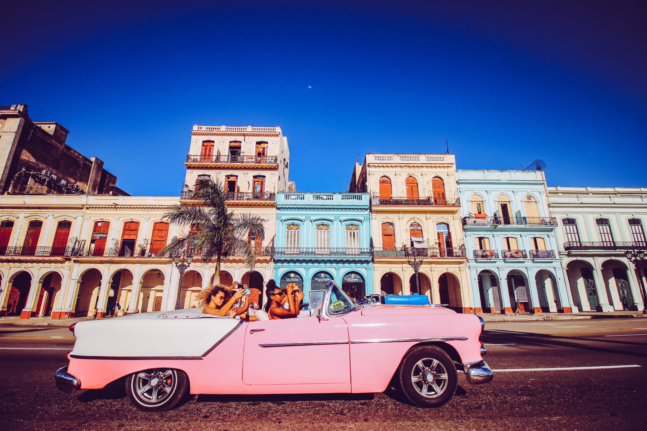 Pink cadillac car with tourists drives past colonial homes in Old Havana